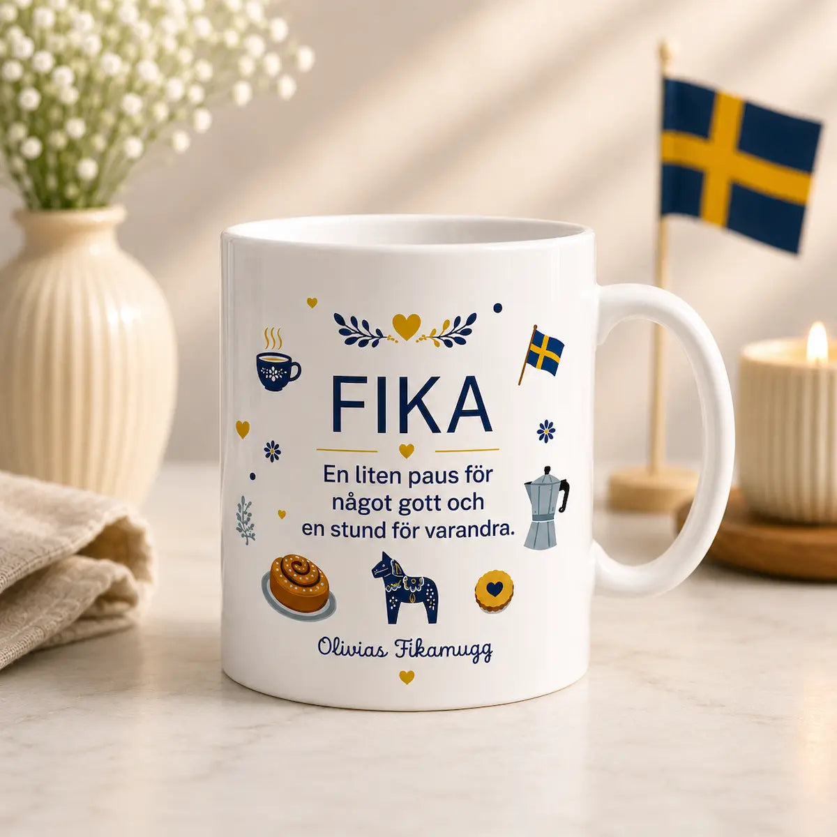 White mug with 'FIKA' text and illustrations on a table with decorative items.